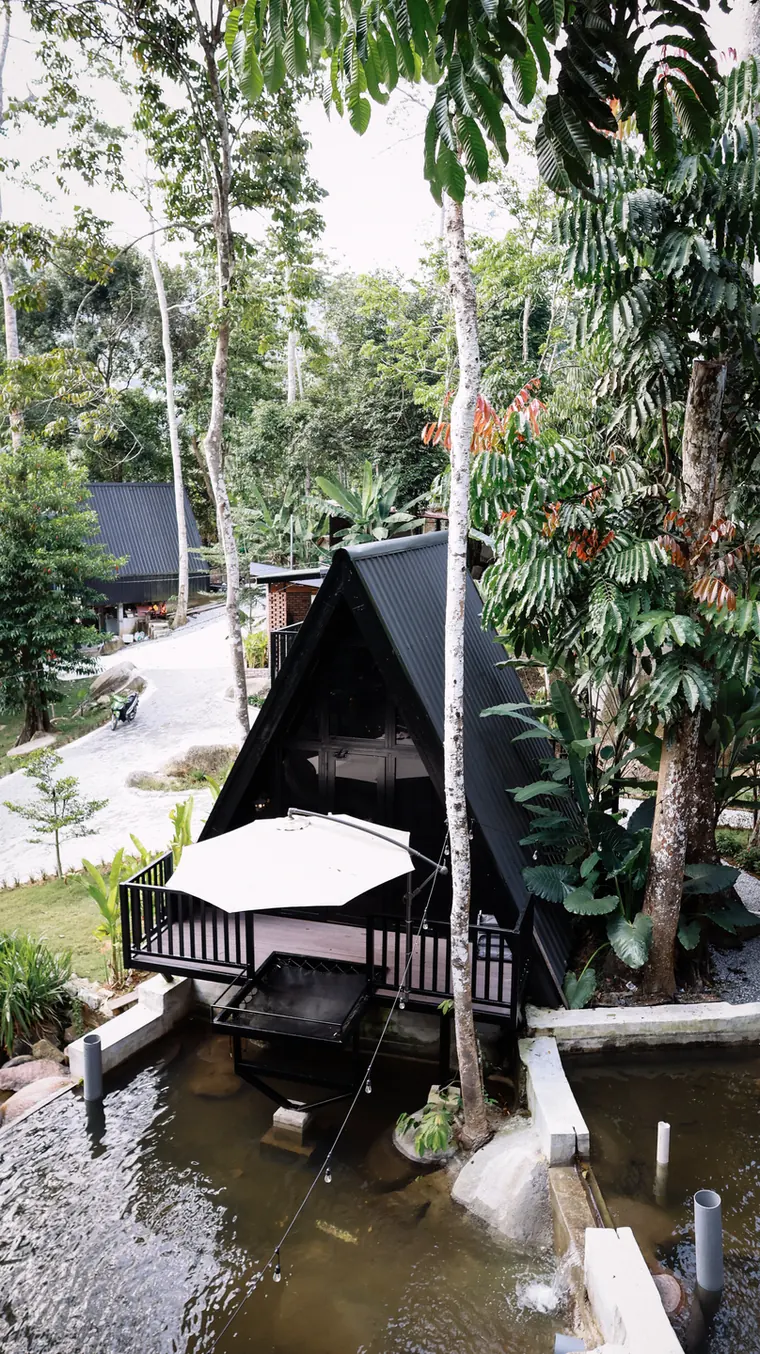 Daylight view of the A-frame resort beside trees and river boulders